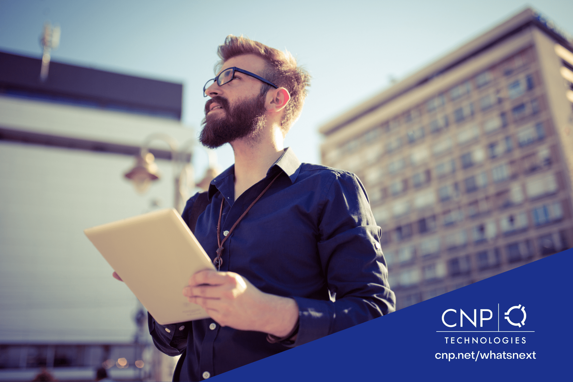 A man is outside looking up toward something while holding a tablet. There are buildings in the background around him. The CNP Technologies logo is in the bottom right corner